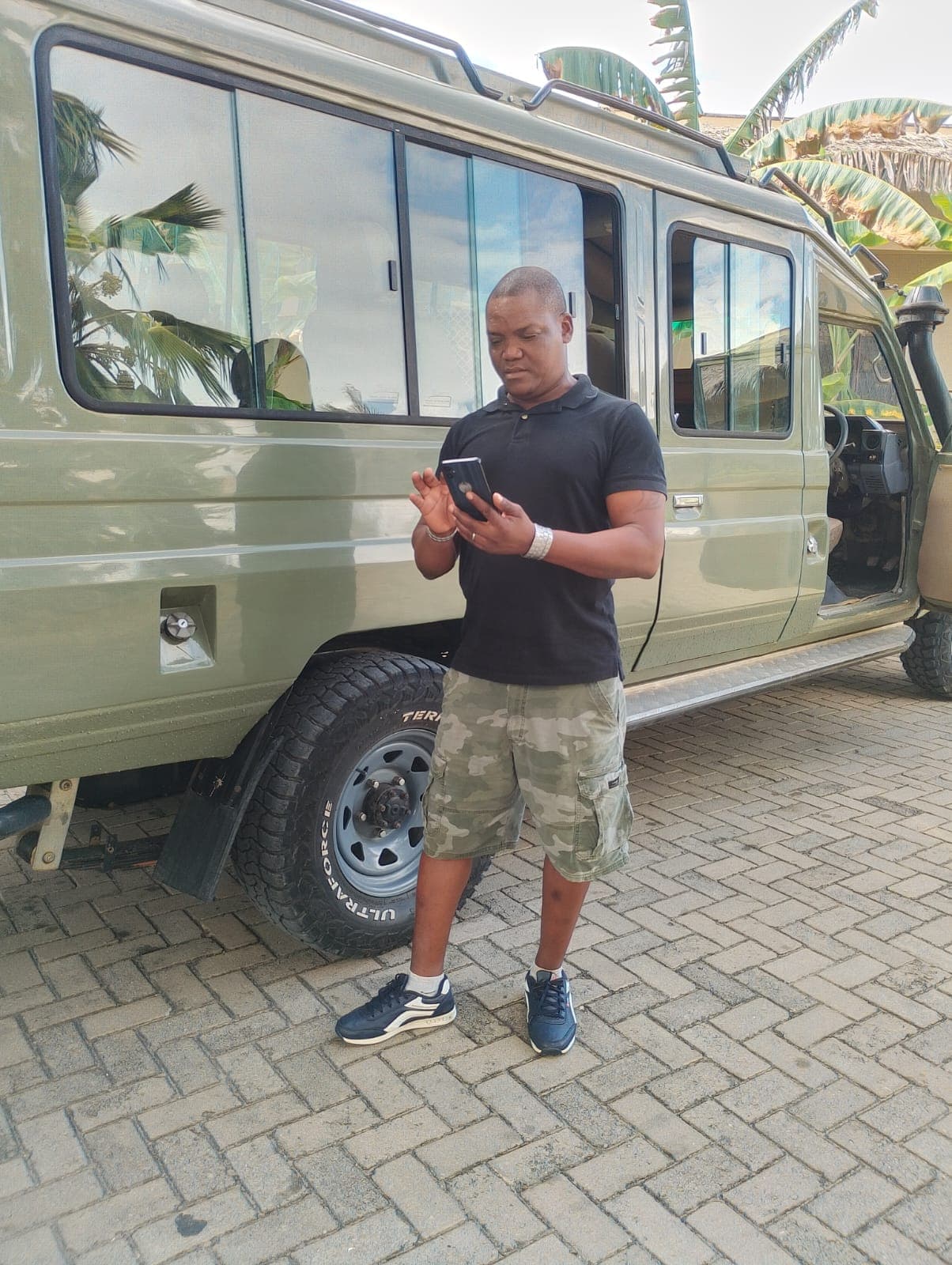 Alfonze Kazungu checking his phone beside his safari vehicle